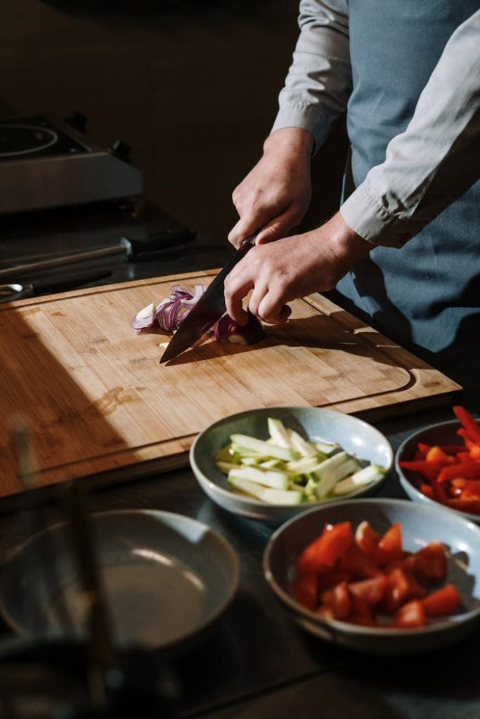 Person Slicing Vegetable on Chopping Board