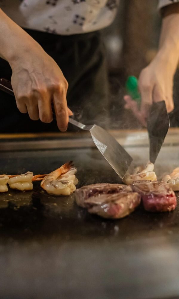 Teppanyaki chef cooking meat and vegetables on a flat-top hibachi grill