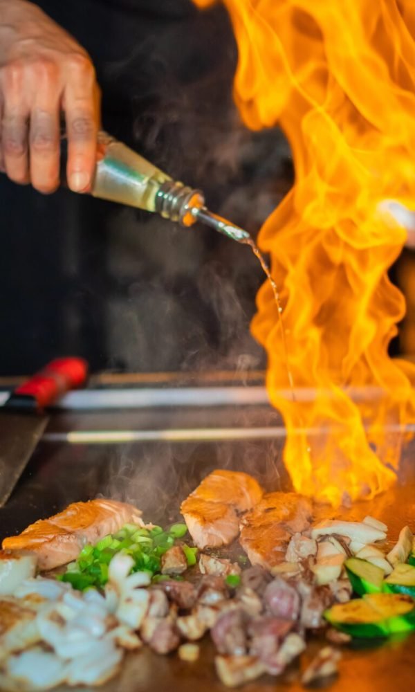 Hibachi chef cooking with a burst of flame on a teppanyaki griddle